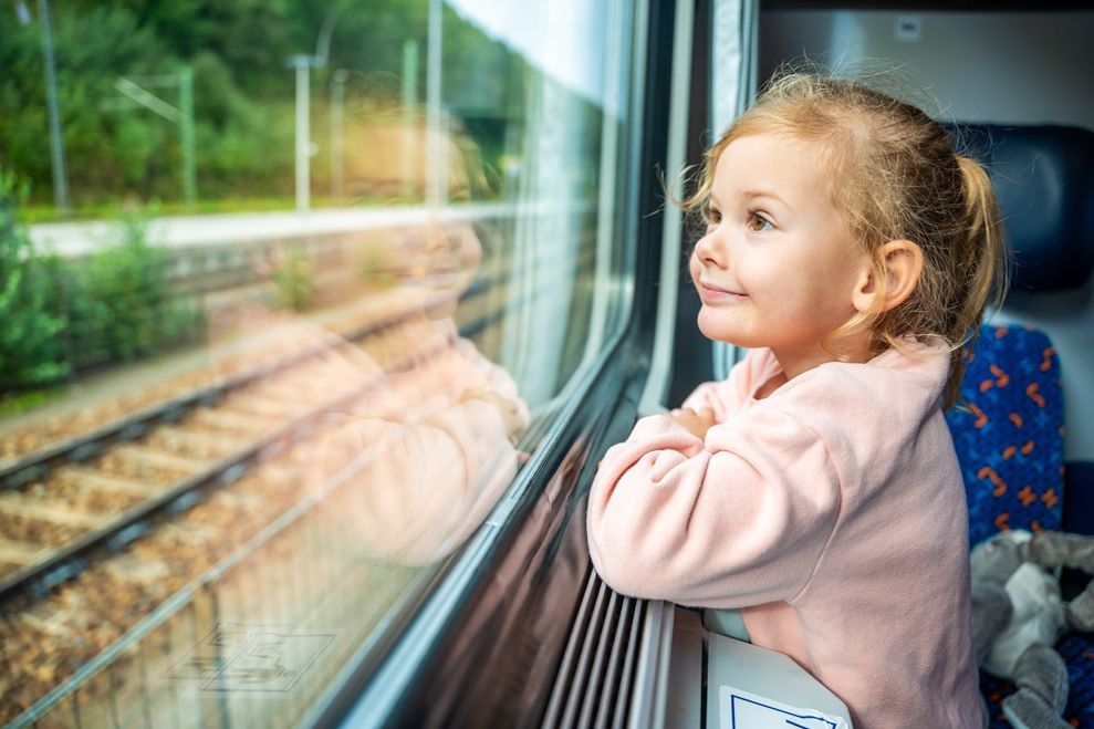 Happy little girl looking out train window outside, while it moving. Traveling by railway in Europe